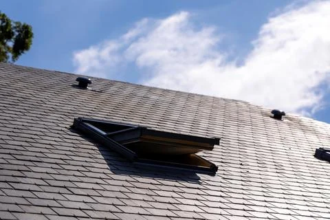 A portrait of an opened skylight window in a slate roof on a sunny day with a Foto stock