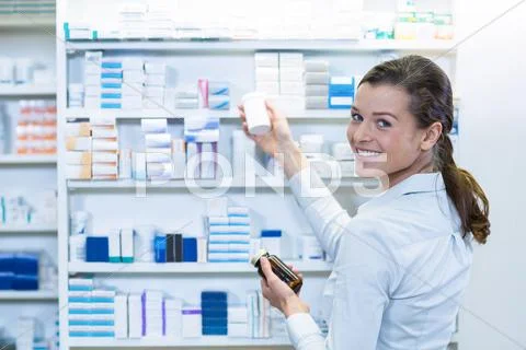 Portrait Of Pharmacist Checking Medicine In Shelf At Pharmacy
