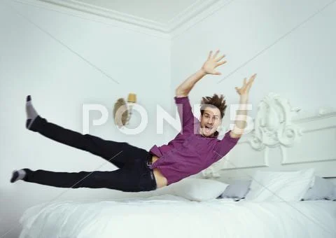 Portrait playful man jumping onto bed Stock Photos