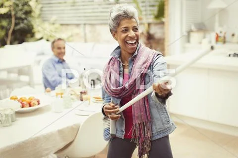 Portrait playful mature woman playing air guitar with stick in kitchen Stock Photos
