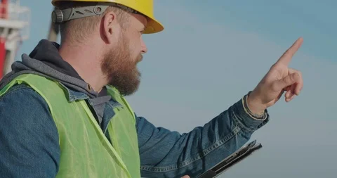 A Portrait Port Worker With A Beard In A Yellow Helmet, Works With A Tablet PC Stock Footage 121660707