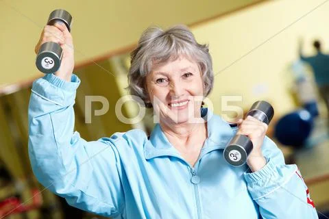 Portrait of positive senior woman lifting dumbbells, looking at camera and smili Stock Photos