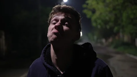 Portrait of positive young guy making funny face and aping on the wet street at Video stock 108005967