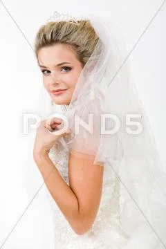 Portrait of pretty bride wearing veil and touching it while looking at camera Stock Photos