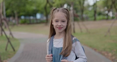 Portrait of pretty junior schoolgirl with backpack stands in spring park Stock Footage 346622145