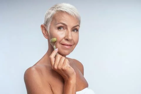 Portrait of a pretty lady smiling using jade roller on her face Foto stock
