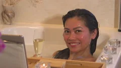Beautiful girl in a bathtub with candles in glasses on the floor and fluffy  feathers on a white table. Stock Video Footage by ©petrunine #325087296