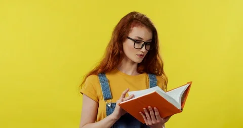 Portrait of the pretty red-haired young girl student in glasses flipping pages Stock Footage 105424407