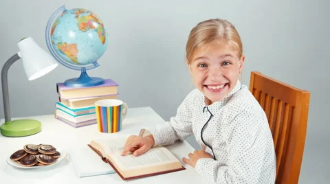 Portrait pupil girl reading a book and laughing. Child sitting at the table Stock Footage