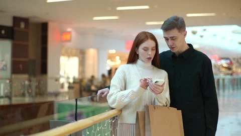 Portrait of puzzled young couple looking for store in shopping mall centre Stock Footage 166016623