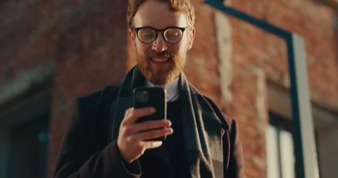 Portrait of a red-haired gorgeous man in glasses using his mobile phone Stock Footage 240116606