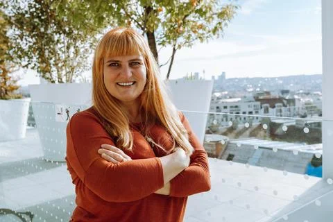 Portrait red-haired middle-aged woman against blurred cityscape background Stock Photos
