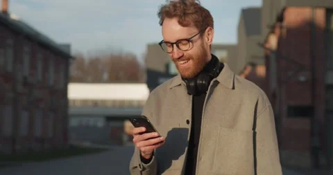 Portrait of a redhead guy in glasses using smartphone while walking on street. Stock Footage 240116228