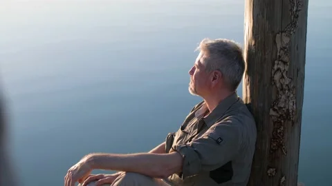 Portrait of a relaxed middle aged man sitting next to lake or sea during sunset. Vídeos de archivo 151394409