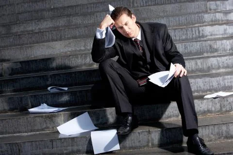Portrait of sad businessman sitting on stairs with papers in hands and lost expr Stock Photos