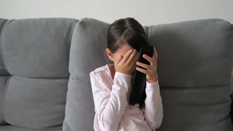 Portrait scared little kid while watching TV. Young Girl sit on sofa and watch Video stock 218370784
