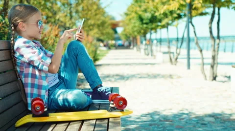 Portrait school girl 7-8 years using smartphone and sitting on the bench Stock Footage