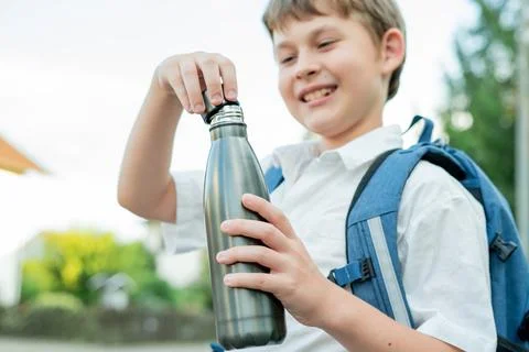 Portrait of a schoolboy with a backpack opens an iron bottle of water. Back t Foto stock