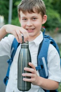 Portrait of a schoolboy with a backpack opens an iron bottle of water. Back t Stock Photos