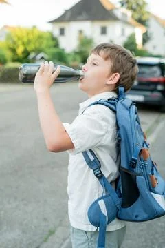 Portrait of a schoolboy with a backpack opens an iron bottle of water. Back t Stock Photos