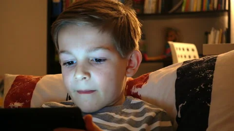 Portrait of schoolboy playing with tablet in bed in the night Stock Footage 134557900