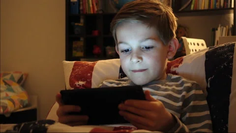 Portrait of schoolboy playing with tablet in bed in the night Stock Footage 134574811