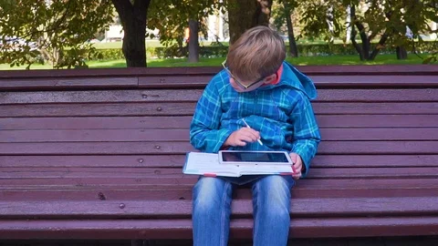Portrait of a schoolboy who does homework with a textbook and a tablet on the Видео 89218178