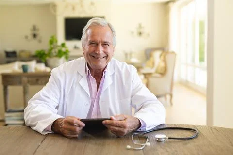 Portrait of senior caucasian male doctor sitting at table using tablet computer Stock Photos