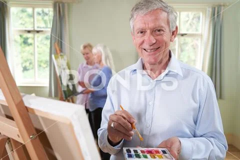 Portrait Of Senior Man Attending Painting Class With Teacher In Back Stock Photos