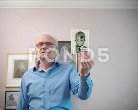 Portrait Of Senior Man Holding Photograph Of Younger Self