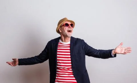 Portrait of a senior man with red sunglasses in a studio, arms stretched. Stock Photos