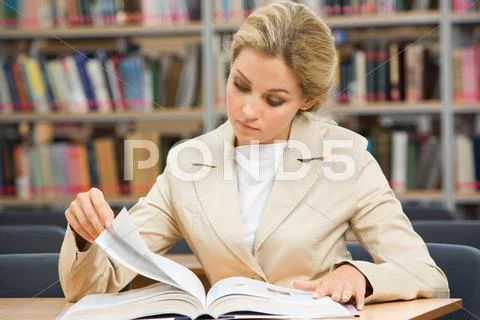 Portrait of serious female leaning over book in the library and reading it Stock Photos