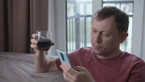 Portrait of serious man sitting on sofa with glass of drink and reading messages Stock Footage 155388791
