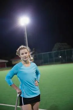 Portrait serious young female field hockey player on field at night Stock Photos