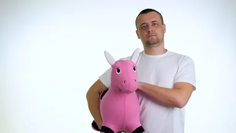 Portrait of serious young man stroking pink toy horse on a white background. Stock Footage 128179367