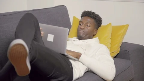 Portrait of serious young student lying with laptop on couch Stock Footage 101428989