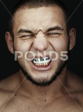 Portrait of shirtless angry young man clenching teeth with message in mouth Stock Photos