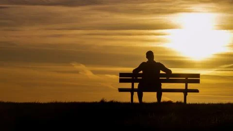 Portrait of a silhouette man sitting on a bench looking towards the sunset, with Stock Photos