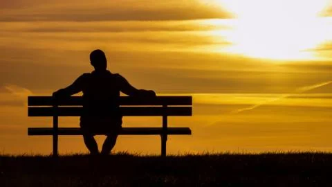 Portrait of a silhouette man sitting on a bench looking towards the sunset, with Stock Photos