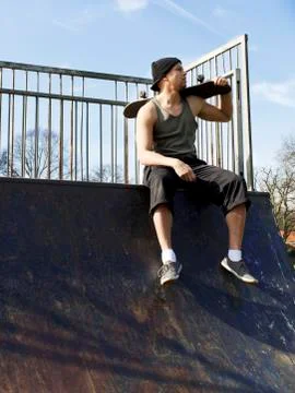 Portrait of a skateboarder sitting on top of a half pipe ramp Stock Photos