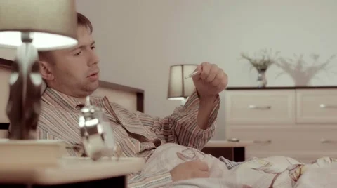 Portrait of sleepy man checking his fever lying in bed Stockbeeldmateriaal 68421205