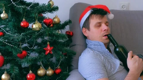 Portrait of sleepy man drinking wine from bottle on couch near Christmas tree. Stock Footage 137807702