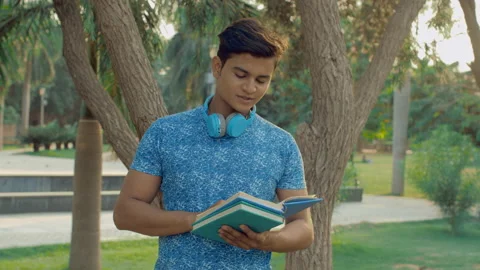 Portrait of a smart boy reading an interesting book while standing under a tree Stock Footage 154297414
