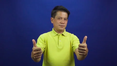 Portrait of smart middle-aged asian man in yellow T shirt showing thumb up Stock Footage 219469096