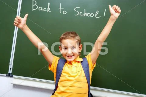 Portrait of smart schoolchild with raised arms by the blackboard looking at came Stock Photos