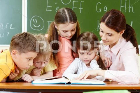 Portrait of smart schoolchildren and their teacher reading book in classroom Stock Photos