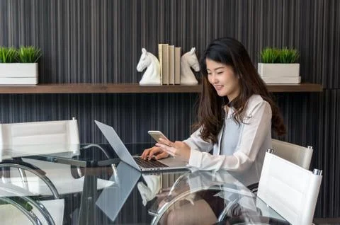 Portrait of smiling asian beautiful young businesswoman sitting at workplace  Stock Photos
