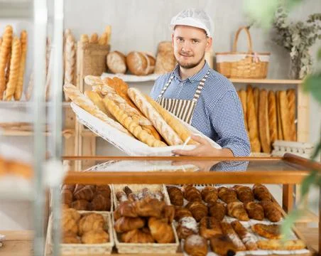 Portrait of smiling baker with fresh bread and baguettes at bakery Stock Photos