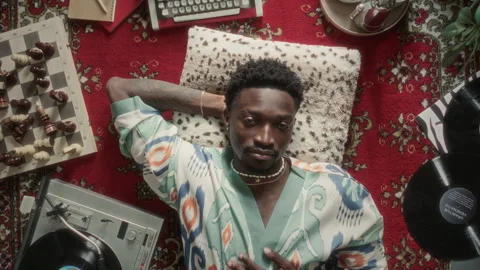 Portrait of Smiling Black Man in Patterned Robe Relaxing on Retro-Style Carpet Stock Footage 339852979