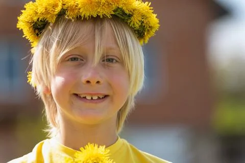 Portrait of smiling blond boy with wreath of dandelions and bouquet of flower Стоковые фото